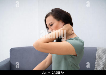 Donna con dolore al collo seduti a casa Foto Stock