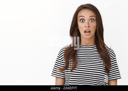 Sorpreso senza parole carine brunette girl in striped t-shirt mascella caduta da stupore, guardare fotocamera vedere incredibile promo, affannosa stupito gli occhi di popping Foto Stock