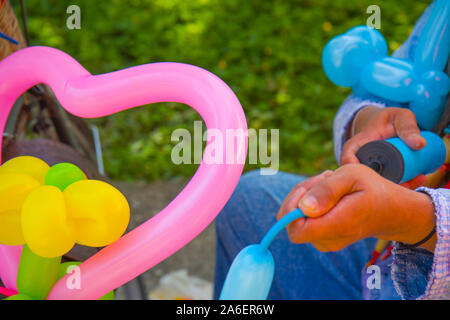 Un clown freelance creazione di palloncini e forme diverse al festival all'aperto nel centro citta'. Borsa Scuola, ali d'angelo, farfalle e cani Foto Stock