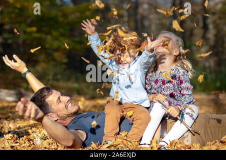 Felice papà e bambini che giocano con le foglie di autunno in foresta Foto Stock