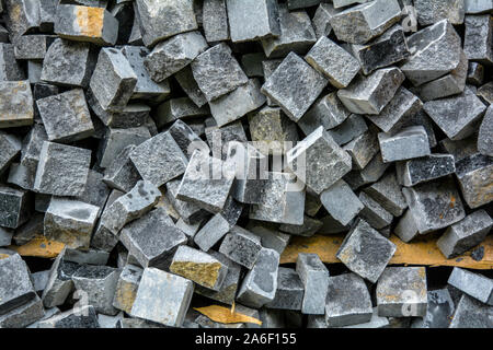 Pila di nera pietra naturale cubi per rendere pavimento esterno di piastrelle. Cataste caotiche di rotture di piastrelle su strada. Costruzione sullo sfondo di un pasticcio bac geometrica Foto Stock