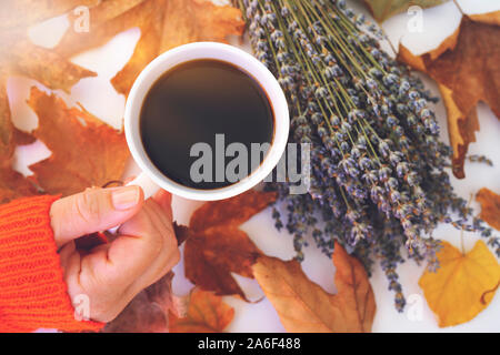 Femmina tenuta a mano tazza di caffè con foglie di autunno e di profumo di lavanda in legno bianco sullo sfondo della tabella Foto Stock