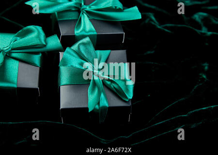 Nero di lusso confezioni regalo con nastro verde risplendere su sfondo di velluto. Natale, festa di compleanno presenta. Padre giorno. Lay piatto. Copia dello spazio. Vista dall'alto. Foto Stock