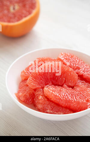 Pompelmo rosso fette in una ciotola bianco su bianco sullo sfondo di legno, vista laterale. Close-up. Foto Stock