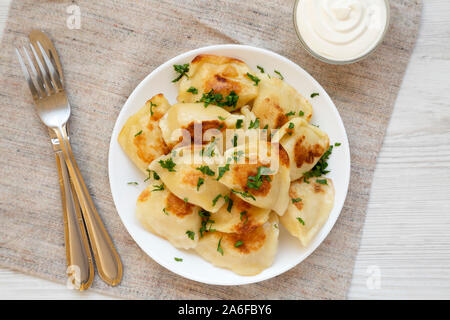 In casa tradizionale polacca di patate fritte pierogis su una piastra bianca con panna acida, vista aerea. Vista in pianta da sopra, piatto laici. Primo piano. Foto Stock