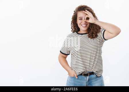 Ragazza vedere solo i lati luminoso. Positivo affascinante bella sorridente chubby giovane studentessa curly-pelose mostra ok ok nessun problema segno sopra gli occhi Foto Stock