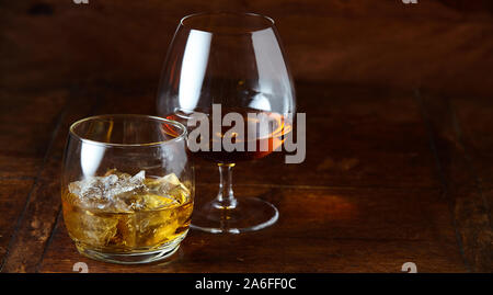 Whisky on the rocks e cognac in un snifter in piedi su una tavola di legno banco bar di notte con spazio di copia Foto Stock