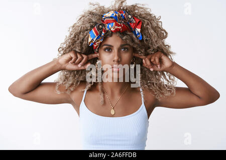 La ragazza si rifiuta sentire bugie. Grave-cercando determinato afro-donna americana con ricci capelli biondi, in abito elegante, chiudere le orecchie con le dita, guardare Foto Stock