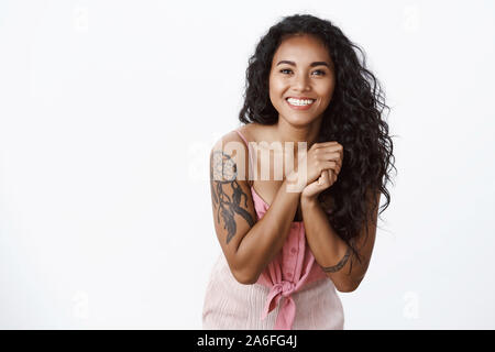 Vita-up shot eleganti bella americano africano a ricciolo femmina dai capelli con tatuaggi, nessuna macchia, inclinare la testa sorridendo grato, guardare e toccato Foto Stock