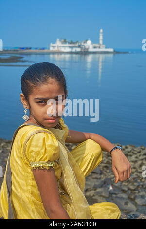 Una giovane ragazza indiana in abito tradizionale seduta da Worli Bay, Mumbai, India, con il punto di riferimento Haji Ali moschea e Dargah in background Foto Stock