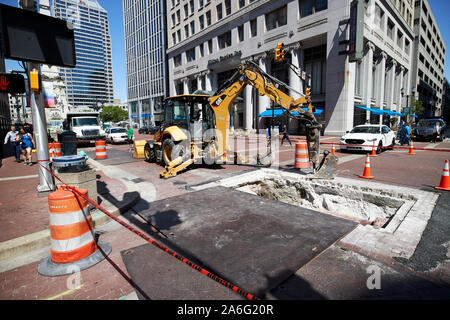 Escavatore cat scava in strada in centro città per utility Indiana Indianapolis USA Foto Stock