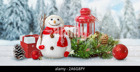 Carino il Natale Capodanno scena con un pupazzo di neve, doni, lanterna, sfere, coni e rami di abete. Inverno, la neve e gli alberi in background. Foto Stock