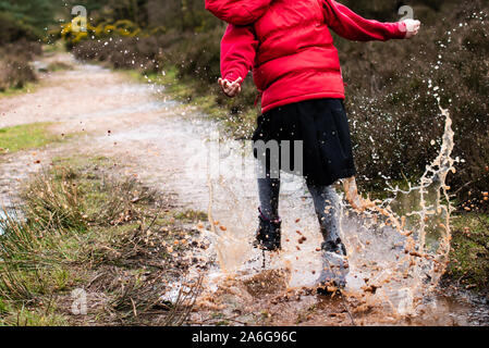 Una bambina cammina, corre e salta attraverso e in molto fangoso pozzanghere in campagna su una famiglia a piedi indossando un caldo corpo rosso più caldo Foto Stock