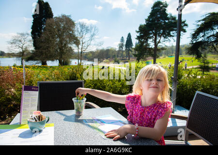 Un simpatico bambina indossa un abito grazioso gode facendo alcune colorazioni in attesa per la sua cena per arrivare, mangiare all'aperto sotto il sole Foto Stock