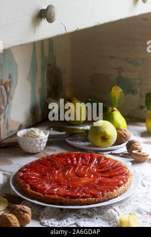 Mela cotogna Tarte tatin servito con panna montata, cotogne frutta e noci su una superficie di legno. Stile rustico. Foto Stock
