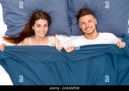 Andare a dormire. Coppia giovane sdraiato sul letto sotto coperta vista superiore sorridendo felice Foto Stock