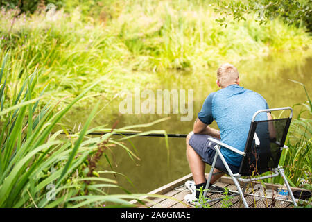 Un uomo pesci pacificamente su una calda giornata d'estate al Lago nel Derbyshire Peak District, tranquillo, Callow Top, Ashbourne Foto Stock