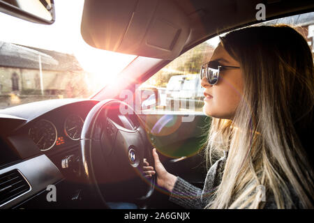 Una giovane donna alla guida di una BMW Serie 5 automobile indossando occhiali da sole in una calda giornata di sole Foto Stock