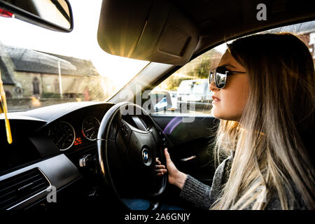 Una giovane donna alla guida di una BMW Serie 5 automobile indossando occhiali da sole in una calda giornata di sole Foto Stock