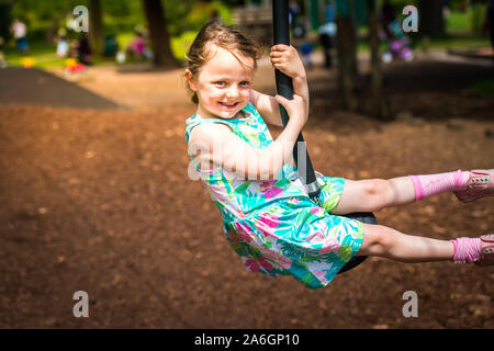 Un simpatico bambina in una luminosa abiti estivi di mangiare un gelato e giocare sulle altalene a Trentham Gardens in una calda giornata d'estate Foto Stock