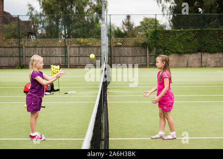 Due giovani ragazze che praticano la loro abilità di tennis presso il locale tennis club, corte Foto Stock