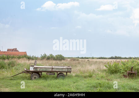 Vecchie e arrugginite, carrello vuoto, in piedi accanto a un campo durante un pomeriggio nuvoloso in Uljma, un piccolo villaggio serbo di Vojvodina, la maggior parte dei prodotti p Foto Stock