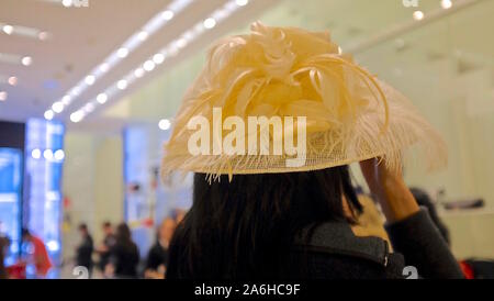 Retro della testa di donna indossando grande giallo pastello canestro con cappello di piume, all'interno luminoso spazio pubblico Foto Stock