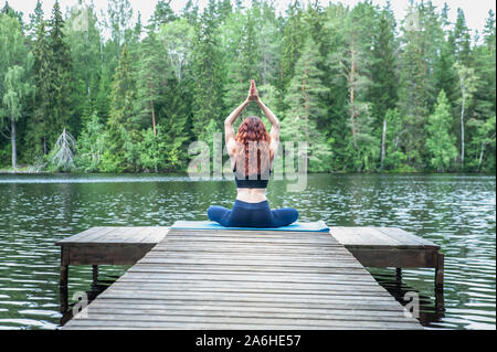 Giovane donna fare yoga sul molo di un bellissimo lago. Concetto di vita sana e naturale equilibrio Foto Stock