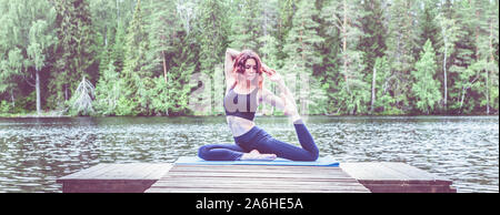 Bella ragazza in un yoga pone sul lago. Eka Pada Rajakapotasana . Uno zampe piccione re pongono . Il concetto di pace, di uno stile di vita sano. Vista panoramica Foto Stock