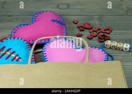 Sacchetto di carta pieno di cuore a mano souvenir e lettere di amore su legno rustico sfondo. Amore, relazione, il giorno di San Valentino, acquisto di concetto di amore Foto Stock