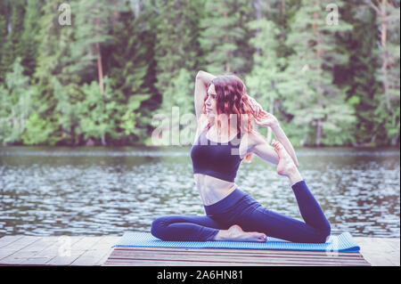 Bella ragazza in un yoga pone sul lago. Eka Pada Rajakapotasana . Uno zampe piccione re pongono . Il concetto di pace, di uno stile di vita sano Foto Stock