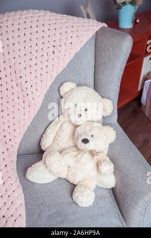 Due bianchi toy orsetti su una sedia e un morbido plaid rosa Foto Stock