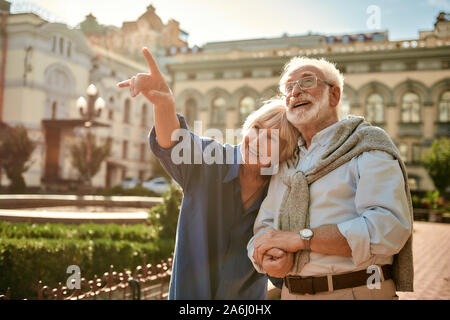 Guardate che! Sorridente donna senior punta lontano e mostrando qualcosa di suo marito mentre spendere tempo insieme all'aperto Foto Stock