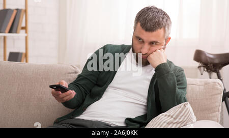 Annoiato uomo canali di commutazione sulla Tv sul weekend Foto Stock