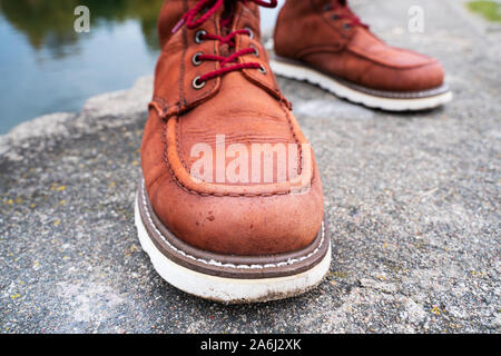 Gocce d'acqua sulla pelle di colore rosso stivali da lavoro di close-up. Il concetto di idrorepellente per impregnazione di scarpe di cuoio Foto Stock