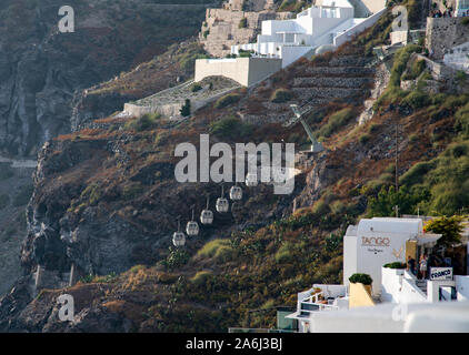 Fira, Grecia - 14 Luglio 2019: Funivia carrelli che scorrono in basso oltre le case e alberghi costruiti molto sul bordo del cliifs di Fira Foto Stock