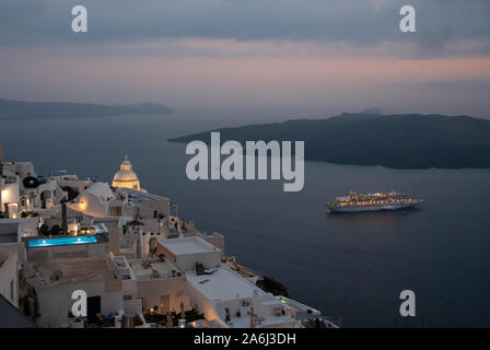 Fira, Grecia - 14 Luglio 2019: Il crepuscolo vista su Fira di alberghi e chiese per la nave da crociera ormeggiata in mare Egeo sotto, preso da Ipapan Foto Stock