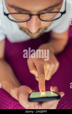 Foto di un piuttosto grave giovane uomo bello premendo qualcosa sul touch screen del suo dispositivo mobile device Foto Stock