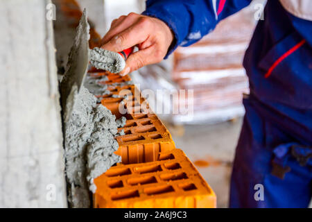 Lavoratore è utilizzando una spatola, cazzuola per applicare la malta su blocchi di colore rosso per rendere al muro, muratore. Foto Stock