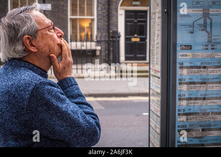 Uomo di mezza età guardando bus tabella di tempo presso la fermata degli autobus Foto Stock
