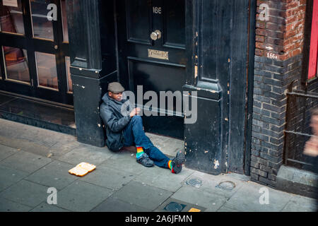 uomo seduto sul pavimento che implora nella porta del negozio Londra Foto Stock