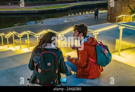 Giovane coppia seduto sui gradini del canale a Coal Drops Yard, King's Cross, Londra Foto Stock