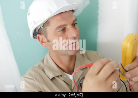 Una mezza età elettricista utilizzando un multimetro Foto Stock