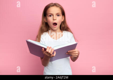 Spaventata ragazza con libro aperto contro sfondo rosa, close up ritratto, isolato sfondo rosa, studio shot. kid ha letto incredibile di informazioni da Foto Stock