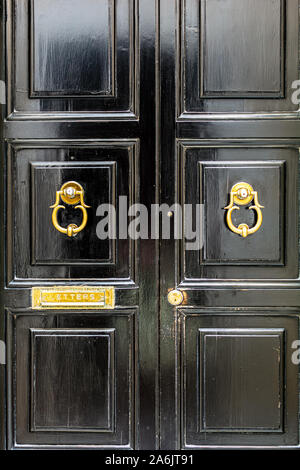 Nero porta in legno con golden vintage spalliere anello sagomato battenti e mail slot letterbox. Porta Nera con golden hardware. Foto Stock
