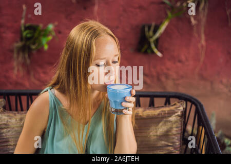 Giovane donna avente una colazione mediterranea seduto al divano e bevande bevanda alla moda: blu del latte. Hot butterfly pea latte o blue spirulina latte Foto Stock
