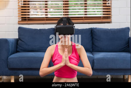 Giovane donna asiatica in realtà virtuale bicchieri fa Yoga e Aerobica a casa,futuro concetto tecnologico. Foto Stock