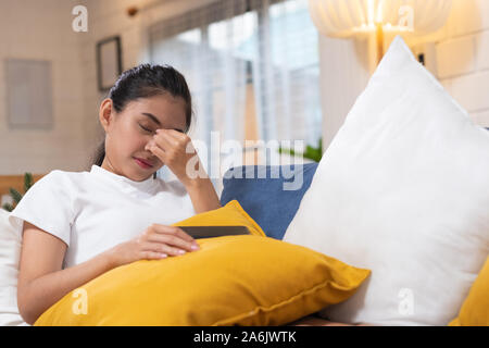 Giovane donna asiatica sensazione lo stress e gli occhi chiusi che soffrono di mal di testa e sdraiato sul divano nel soggiorno,femmina stanco lavoratore di ufficio massagin Foto Stock