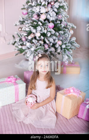 Anno Nuovo 2020! Il concetto di Natale, vacanze e dell'infanzia. Una piccola ragazza in un abito rosa detiene un giocattolo musicale giostra vicino a un albero di Natale. Foto Stock