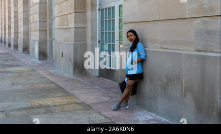 Donna asiatica in sneakers, gonna e giacca blu appoggiata contro l edificio in cemento Foto Stock